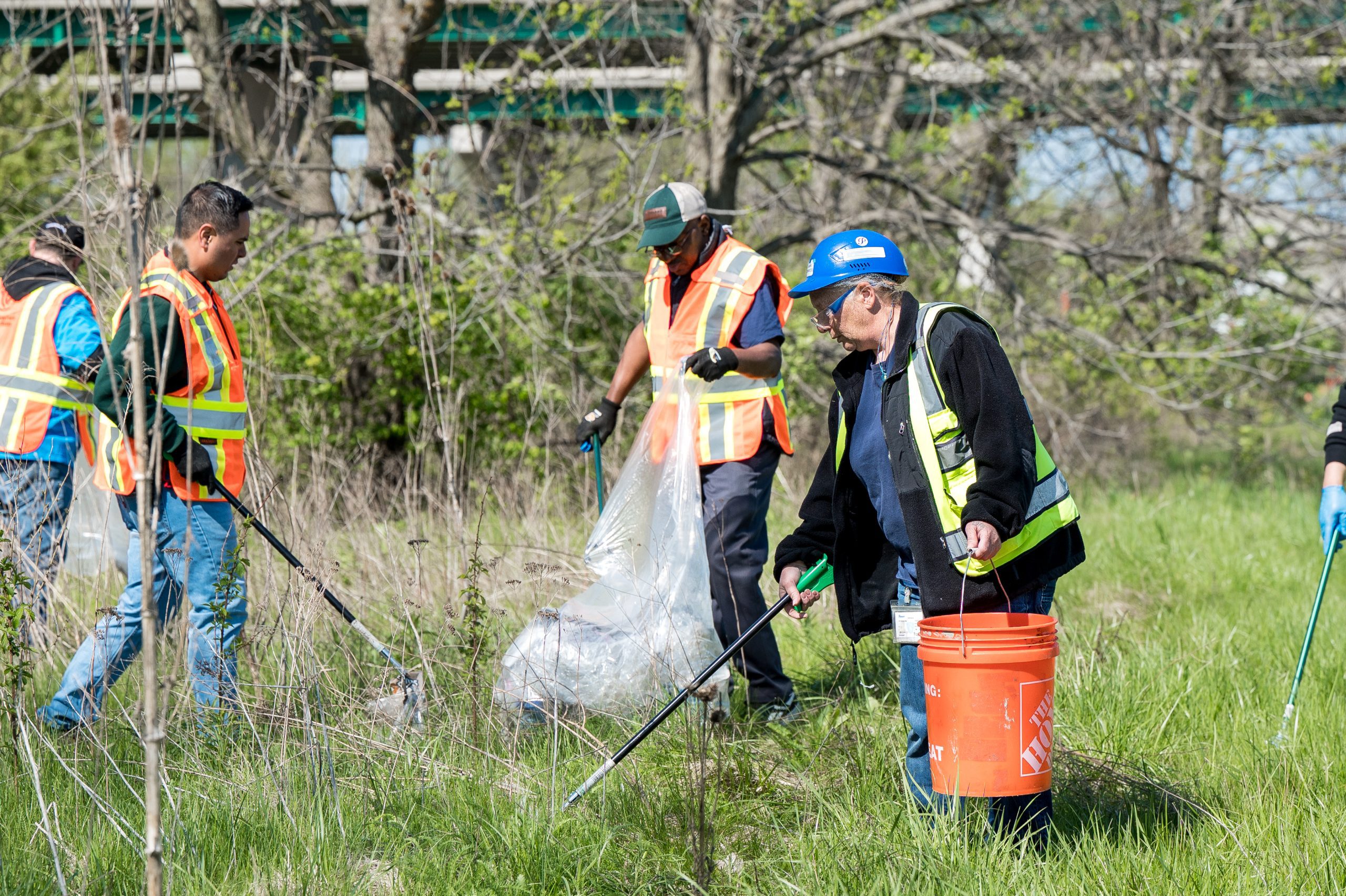 Plastipak employees from the Champaign facility pose together during an Adopt-a-Highway roadside cleanup event, holding collected trash bags and safety equipment while supporting community beautification efforts.